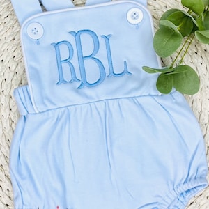 May include: Light blue baby romper with white trim and a monogrammed "RBL" in blue thread. The romper has a gathered skirt and snaps at the bottom.