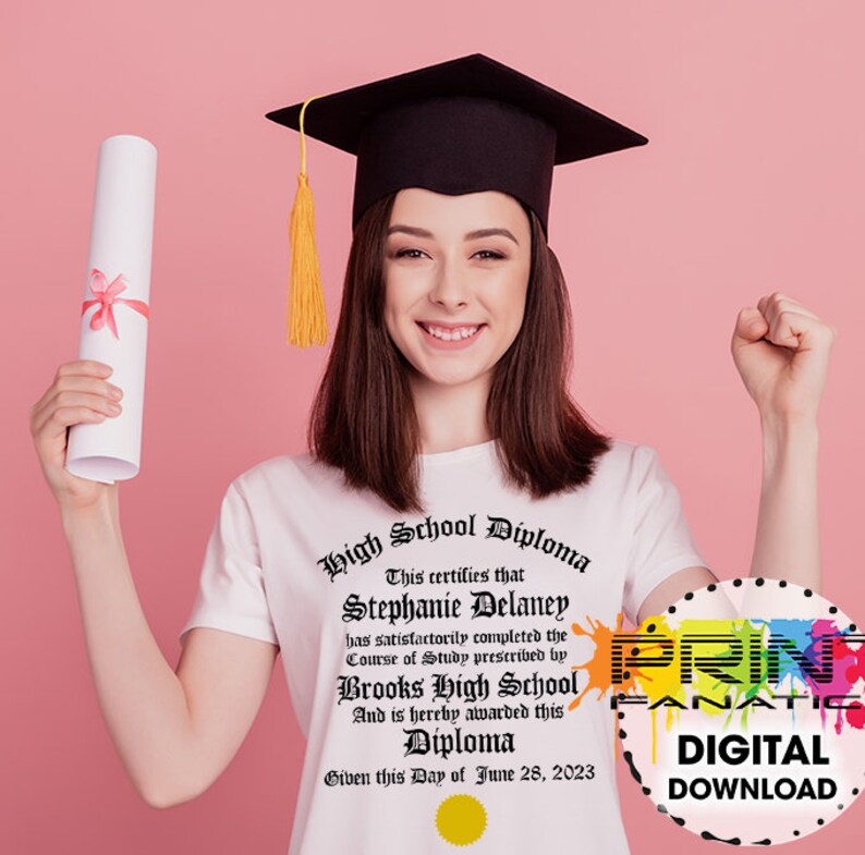 Puede incluir: Una persona con birrete y camiseta blanca con dise&ntilde;o de diploma. La camiseta dice "High School Diploma" e incluye nombre, escuela y fecha. Un diploma enrollado atado con una cinta rosa se sostiene en una mano.