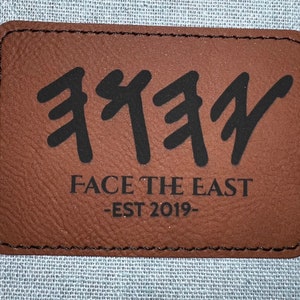 May include: Brown leather patch with black stitching and the text "FACE THE EAST -EST 2019- " and a stylized black graphic of three "F" letters.