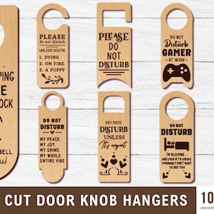 May include: A collection of ten laser-cut wooden door knob hangers. Designs include "Do Not Disturb" messages with various themes, such as "Baby Sleeping," "Gamer at Work," and "Mom is Working." Each hanger has a unique shape and text.