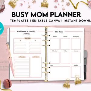 以下が含まれることがあります： 「BUSY MOM PLANNER」と「TEMPLATES I EDITABLE CANVA I INSTANT DOWNLOAD」のテキストが書かれたピンクのプランナー。プランナーには、「Semi Annual & Annually Cleaning」と「This Week」のセクションがあります。