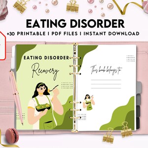 May include: A pink binder with a green and white cover featuring the text "Eating Disorder Recovery". The cover also includes a cartoon illustration of a person eating a salad. The binder has a gold ring binding and a blank page with the text "This book belongs to:" at the top.