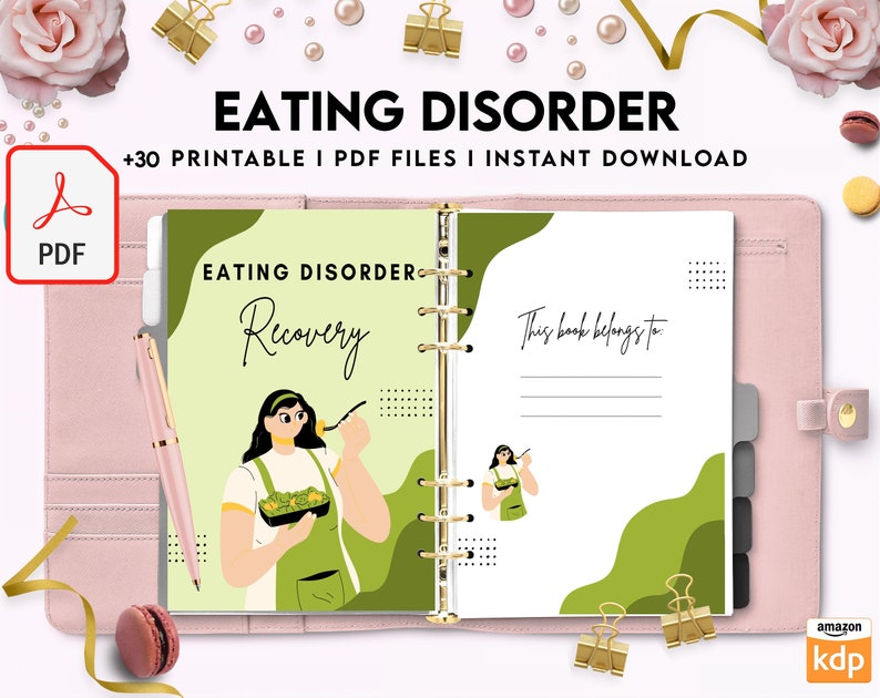 May include: A pink binder with a green and white cover featuring the text "Eating Disorder Recovery". The cover also includes a cartoon illustration of a person eating a salad. The binder has a gold ring binding and a blank page with the text "This book belongs to:" at the top.