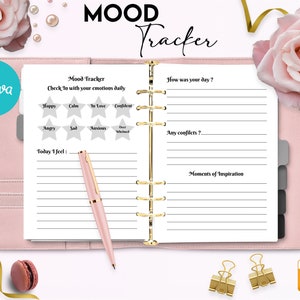 May include: A pink and white planner with a gold spiral binding. The cover says "MOOD Tracker" and has a pink rose on the right side. The inside pages have lines for writing and a section for tracking moods with stars.