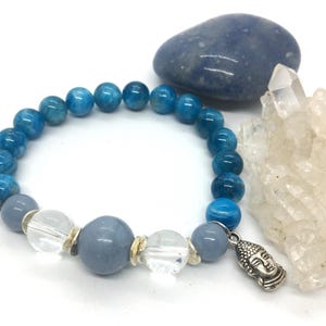 May include: A blue and grey gemstone bracelet with a silver Buddha charm. The bracelet is made with round beads and has clear crystal beads interspersed throughout.