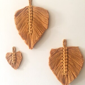 Puede incluir: Tres tapices de macram&eacute; en forma de hojas, hechos con un cord&oacute;n marr&oacute;n natural. La hoja m&aacute;s grande est&aacute; en la parte superior, y la hoja m&aacute;s peque&ntilde;a est&aacute; en la parte inferior.
