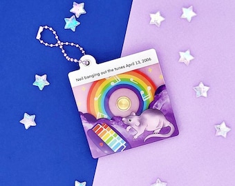 May include: A purple and rainbow keychain with a cartoon rat playing a keyboard. The keychain has the text "Neil banging out the tunes April 13, 2006".