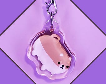 May include: A clear acrylic keychain featuring a cartoon Shiba Inu dog with brown and white fur. The keychain has a silver metal clasp.