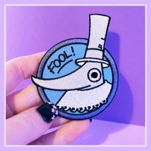 May include: A blue and white embroidered patch featuring a character with a top hat and the word "FOOL!" in a circle.