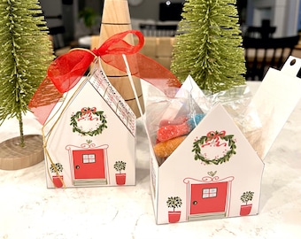 Op de afbeelding: Twee witte kartonnen huisjes met rode deuren en groene kransen. De huisjes zijn versierd met gouden lint en hebben een transparant plastic raam. Eén huisje is open en gevuld met kleurrijke snoepjes.