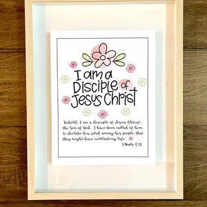 May include: A framed print with a white background and pink and green flowers. The text reads "I am a Disciple of Jesus Christ" and includes a scripture reference from the Book of Mormon: "Behold, I am a disciple of Jesus Christ, the Son of God. I have been called of him to declare his word among his people, that they might have everlasting life." 3 Nephi 5:13