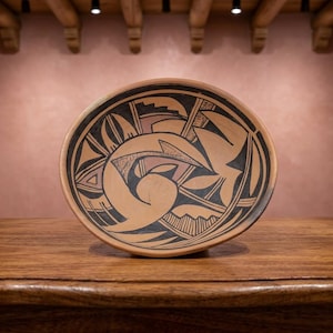 May include: A round ceramic bowl with a terracotta base color featuring intricate black and dark brown geometric patterns. The interior design includes stylized bird-like shapes, curved lines, and stepped motifs painted across the surface.