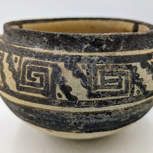 May include: A small, round, black and white ceramic pot with a geometric design. The pot has a wide mouth and a rounded bottom.