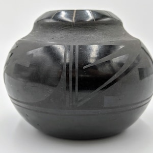 May include: Black pottery vase with a geometric design. The vase is hand-crafted and has a smooth, glossy finish.