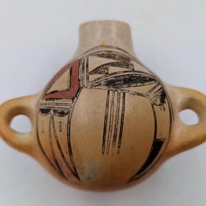 May include: A small, hand-painted ceramic pot with two handles. The pot is decorated with a geometric pattern in black, red, and white.