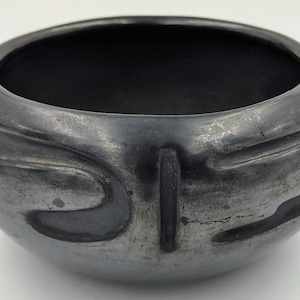 May include: A handcrafted, dark gray ceramic bowl with a rounded shape. The bowl features carved, curved designs around the exterior. The interior is a deep, dark color. This decorative bowl is suitable for home decor.