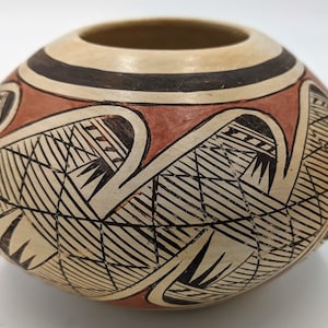 May include: A small, round, hand-painted pottery bowl with a geometric design in black and white on a red background.