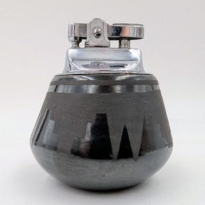 May include: A black ceramic lighter with a silver top and a geometric design. The lighter is shaped like a rounded cone.