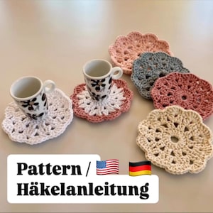 Könnte beinhalten: Fünf gehäkelte Untersetzer in verschiedenen Farben, darunter Weiß, Rosa, Beige, Grau und Hellrosa. Die Untersetzer haben die Form einer Blume mit einem Loch in der Mitte. Zwei Kaffeetassen mit Blumenmustern stehen auf zwei der Untersetzer. Der Text "Pattern / Häkelanleitung" steht unter den Untersetzern.