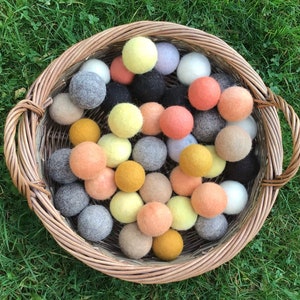 May include: A wicker basket filled with colourful felt balls in shades of yellow, orange, pink, grey, and black. The balls are arranged in a random pattern and are a popular sensory toy for children.