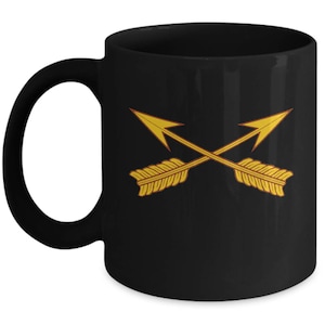 May include: Black ceramic coffee mug with a gold crossed arrows design. The arrows are stylized and have a red outline.