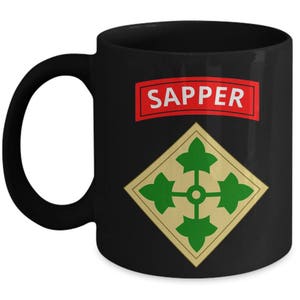 May include: Black ceramic mug with a large handle. The mug features a red rectangle with the word "SAPPER" in white letters. Below the rectangle is a gold diamond shape with green leaf designs.