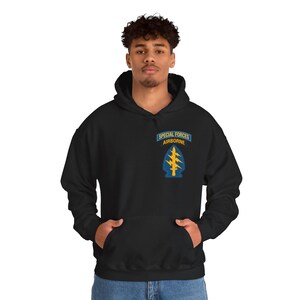 May include: A black hooded sweatshirt featuring an embroidered patch on the upper left chest. The patch displays a blue tab with the text SPECIAL FORCES AIRBORNE in yellow, above a blue arrowhead shape containing a yellow sword and lightning bolts.