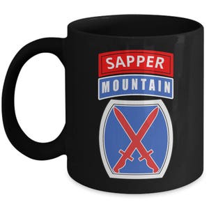 May include: Black ceramic coffee mug with a white and blue military insignia featuring crossed swords and the text "SAPPER MOUNTAIN".