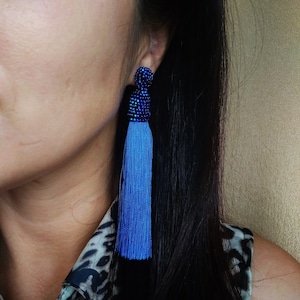 Puede incluir: Un par de pendientes de borla azul con una parte superior de cuentas azul oscuro. Los pendientes cuelgan de la oreja de una mujer.