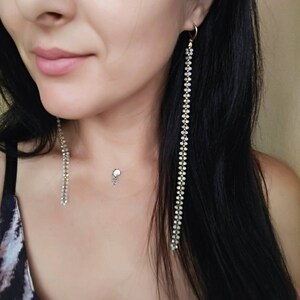May include: A pair of long, dangling earrings with a gold chain and white beads. The earrings are worn by a person with long black hair.
