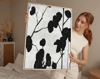 May include: Abstract black and white artwork featuring a botanical design. The painting has a light-colored background with black leaf-like shapes and thin, dark lines. The artwork is framed in a light-colored wooden frame.