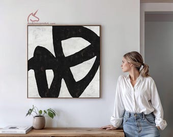 May include: Abstract black and white artwork in a wooden frame. The painting features bold, overlapping black brushstrokes against a textured white background. The artwork is displayed above a wooden cabinet, creating a modern aesthetic.