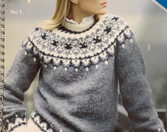 May include: A woman wearing a gray sweater with a patterned yoke and cuffs, and a gray hat. The sweater is from Alafoss lopi, No. 1. The sweater has a white and black design around the neck and cuffs.