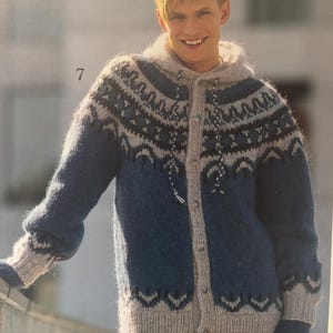 Può includere: Un cardigan con cappuccio blu e grigio con un motivo. Il cardigan ha una chiusura con bottoni e viene indossato con guanti abbinati. I polsini e l'orlo sono grigi. Il capo è in maglia.