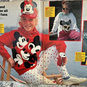 Può includere: Una pagina di rivista con istruzioni per lavorare a maglia dei maglioni con Mickey Mouse e Minnie Mouse. I maglioni sono rossi, bianchi e blu con pois. La pagina della rivista include anche una foto di un bambino che indossa un maglione rosso con Mickey Mouse e Minnie Mouse.