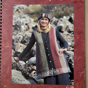 Può includere: Una copertina di un libro di modelli di maglia con una donna che indossa un gilet a righe con un motivo geometrico sul fondo. Il gilet è realizzato con filato Lätt-Lopi. Il libro è intitolato "Lätt-Lopi" ed è pubblicato da Ístex, Íslenskur Textilidnaður hf. Il numero del libro è 13.