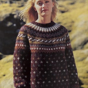Könnte beinhalten: Ein brauner, weißer und goldfarbener Pullover mit Rundhalsausschnitt. Der Pullover ist aus einem dicken, strukturierten Garn gefertigt.
