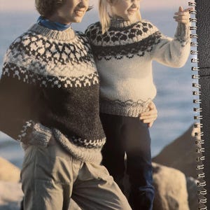 Könnte beinhalten: Zwei Personen tragen passende Strickpullover mit einem geometrischen Muster in Schwarz, Weiß und Grau. Die Pullover haben einen hohen Ausschnitt. Der Text "6-7" befindet sich in der oberen linken Ecke. Der Markenname "Alafoss lopi" befindet sich in der unteren linken Ecke.