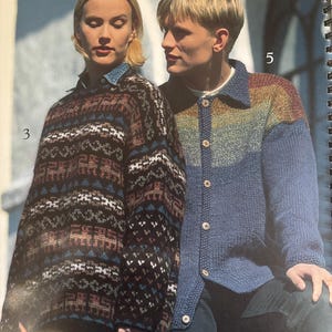 May include: Two people wearing knitted sweaters. One sweater is a dark brown, black, and white patterned design. The other is a blue cardigan with a rainbow-colored upper section. Both sweaters have long sleeves and are button-down.