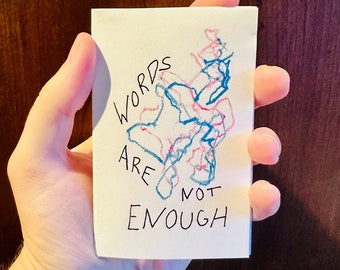 Può includere: Un biglietto bianco con le parole "WORDS ARE NOT ENOUGH" scritte in inchiostro nero. Il biglietto ha un disegno astratto blu e rosa.
