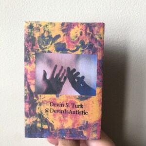 Puede incluir: Un peque&ntilde;o libro colorido con una foto de dos manos que se alcanzan la una a la otra. El libro tiene el texto "Devin S. Turk @DevinIsAutistic" en la portada.