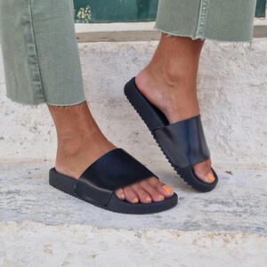 以下が含まれることがあります： 厚いゴム製のソールが付いた、黒い革製のサンダルです。サンダルは、足の甲に1本のストラップが付いたシンプルなデザインです。