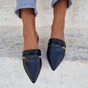 May include: Black leather pointed-toe mules with a cut-out detail and a knotted strap across the vamp.
