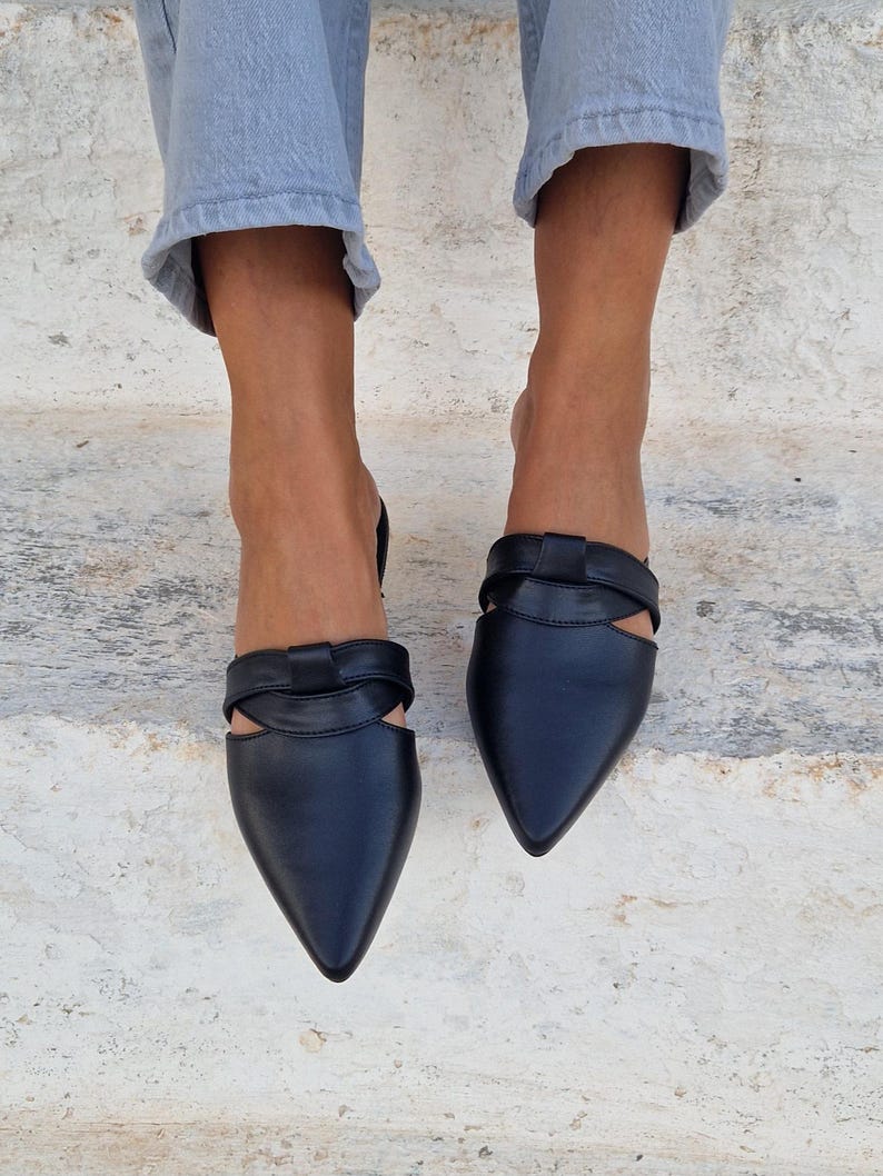 May include: Black leather pointed-toe mules with a cut-out detail and a knotted strap across the vamp.