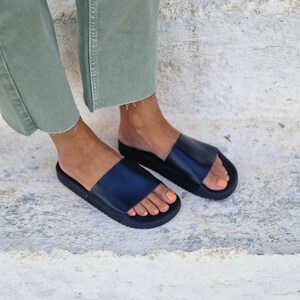 以下が含まれることがあります： 厚底プラットフォームソールが付いた黒い革製のサンダル。サンダルは足に履かれている