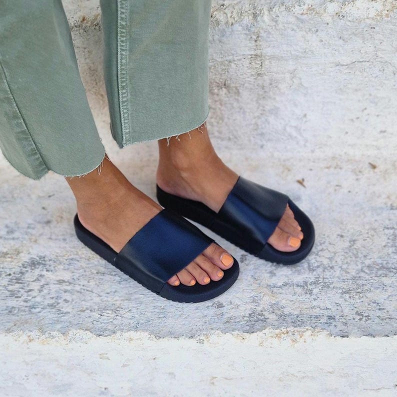 以下が含まれることがあります： 厚底プラットフォームソールが付いた黒い革製のサンダル。サンダルは足に履かれている