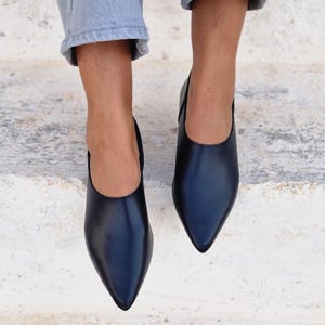 Pode incluir: Um par de sapatos pretos de couro de bico fino com salto baixo. Os sapatos s&atilde;o usados por uma pessoa que est&aacute; vestindo jeans azul claro.