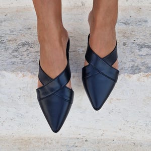 May include: Black leather pointed-toe mules with criss-cross straps.