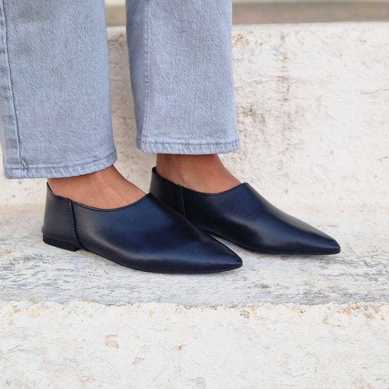 Pode incluir: Um par de sapatos pretos de couro sem cadar&ccedil;os com bico fino. Os sapatos s&atilde;o planos e t&ecirc;m um design simples.