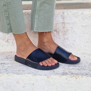 以下が含まれることがあります： 厚い黒いゴム製のソールが付いた黒い革製のサンダル。裸足の人が履いています。